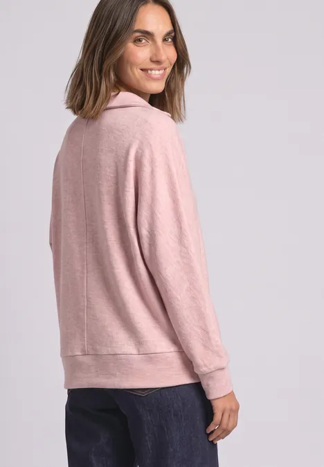 Koszulka Polo z długim rękawem w stylu melanżowym vintage blush mel. Kobieta ma różowy sweter i uśmiecha się patrząc przez ramię.