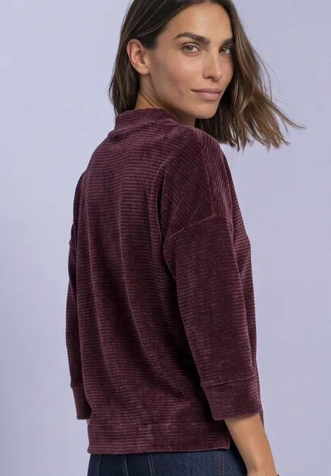 Femme portant un haut velours côtelé bordeaux à manches 3/4, regard par-dessus l’épaule.
