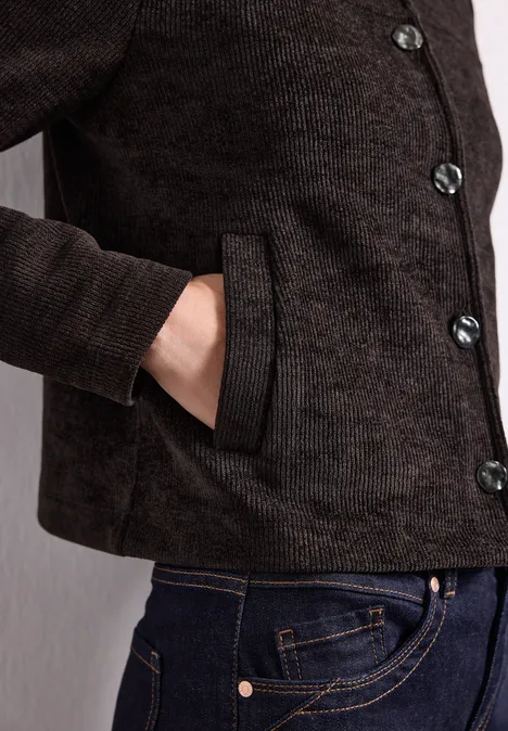 Veste à manches longues, col rond et boutons black coffee Dunkelbraune Jacke mit Knöpfen, Hand in der seitlichen Tasche, dazu blaue Jeans.