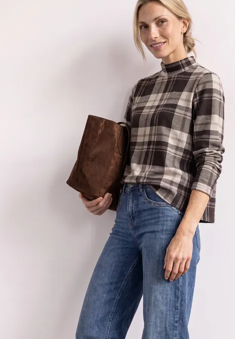 Langarm Shirt mit Turtle Neck und Karomuster black coffee Eine Frau in karierter Bluse und Jeans hält eine braune Tasche unter dem Arm vor hellem Hintergrund.