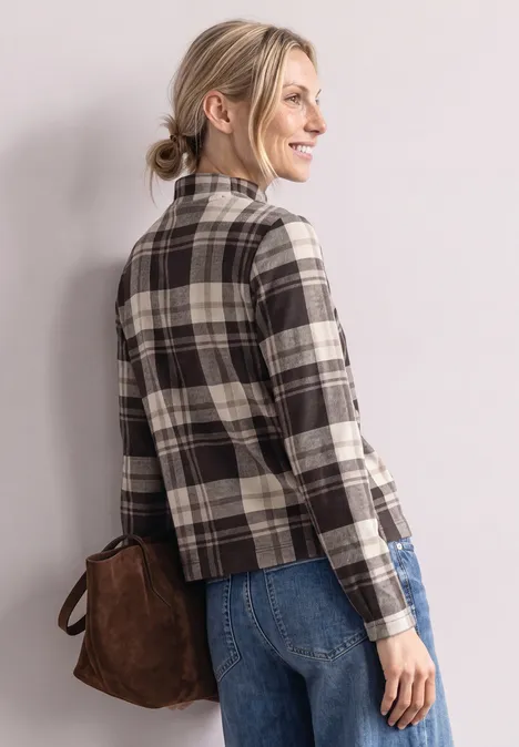 Langarm Shirt mit Turtle Neck und Karomuster black coffee Frau in kariertem Blazer, Jeans und brauner Tasche, lächelnd seitlich nach rechts gewandt.