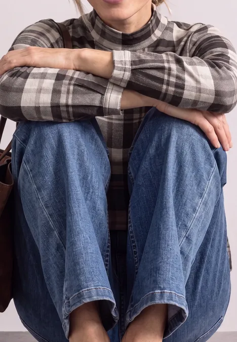 Langarm Shirt mit Turtle Neck und Karomuster black coffee Eine Person sitzt mit verschränkten Armen auf den Knien, trägt eine karierte Bluse und Jeans.