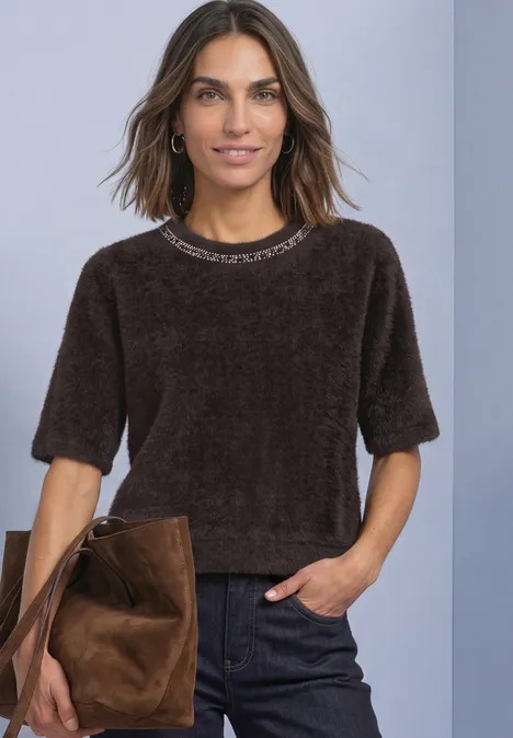 T-Shirt mit Rundhals und Schmucksteinen black coffee Frau mit braunem, samtigem Kurzarmshirt, dunklen Jeans und brauner Wildledertasche vor neutralem Hintergrund.