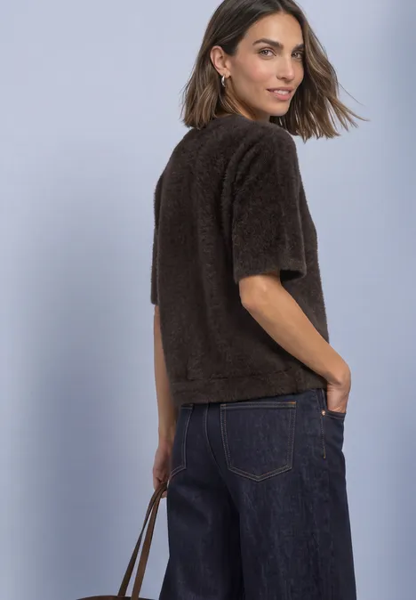 T-Shirt mit Rundhals und Schmucksteinen black coffee Frau im Profil trägt kurzärmligen braunen, flauschigen Pullover, dunkelblaue Jeans und hält eine Tasche.