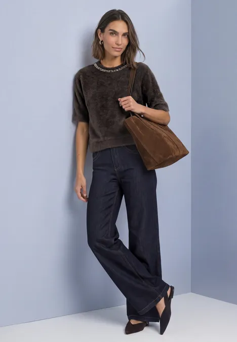 T-Shirt mit Rundhals und Schmucksteinen black coffee Frau in braunem Kurzarmshirt, weitem Jeansbund, schwarzen Ballerinas und brauner Tasche vor hellblauem Hintergrund