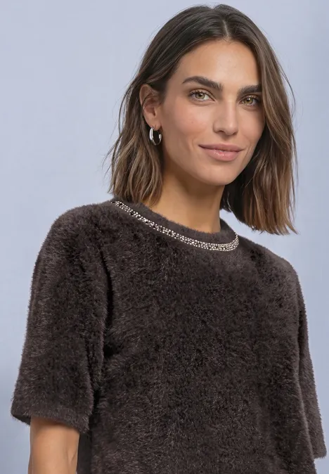 T-Shirt mit Rundhals und Schmucksteinen black coffee Frau mit braunem, flauschigem Kurzarm-Pullover und Ohrringen vor hellem, neutralem Hintergrund.