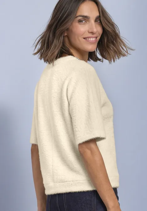 T-Shirt mit Rundhals und Schmucksteinen pure beige Frau trägt cremweißes, kurzärmeliges, flauschiges Shirt, seitliche Rückenansicht vor hellem Hintergrund.