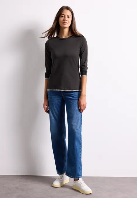 Langarm Shirt mit karierten Meshdetails black coffee Junge Frau steht vor weißer Wand, trägt schwarzen 3/4-Ärmel-Pullover, blaue Jeans und weiße Sneaker.