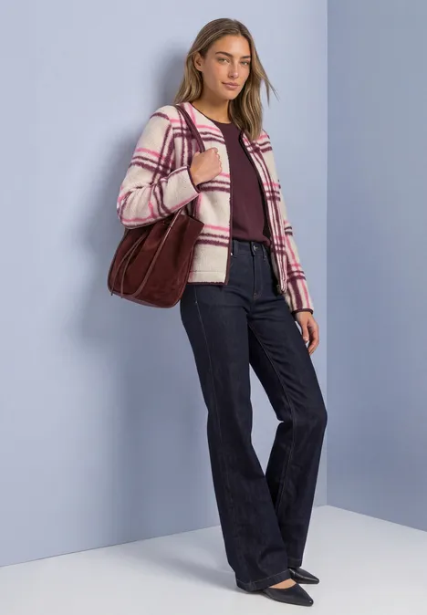 Modisch gekleidete Frau mit weiten Jeans, karierter Jacke und großer roter Tasche vor hellblauem Hintergrund.