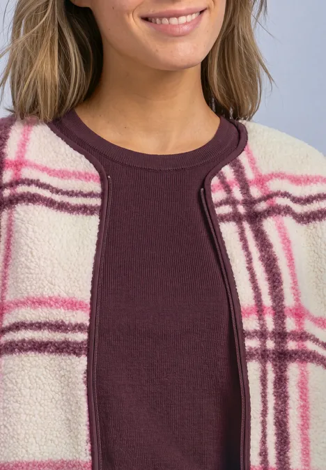 Frau trägt burgunderfarbenes Top unter beiger Fleecejacke mit pink-lila Karomuster.
