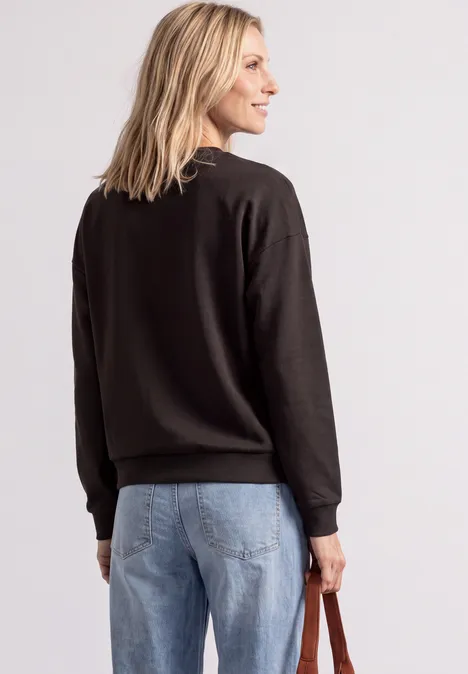 Femme de dos en pull noir et jean, tenant un sac à la main.