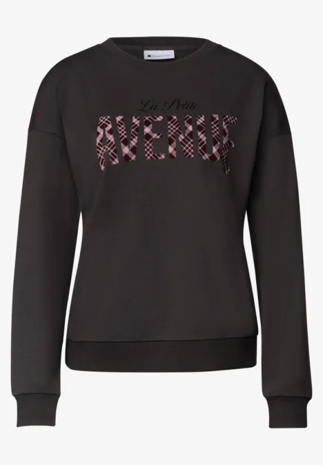 Sweat noir à col rond avec inscription "AVENUE" en motif floral rouge sur la poitrine.