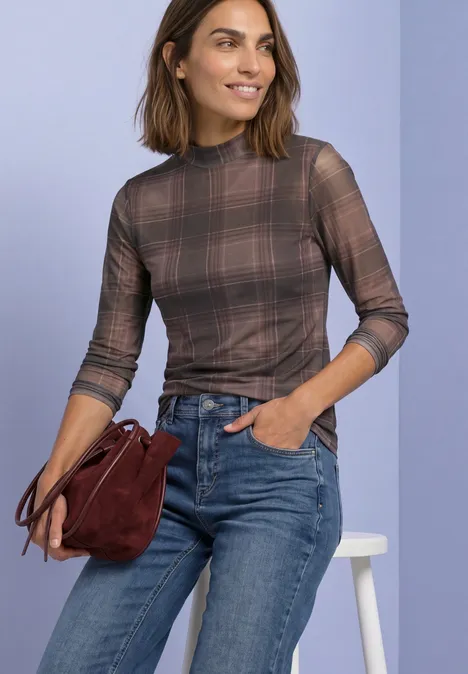 T-shirt à manches longues en mesh, col rond et imprimé sanded amber Frau in kariertem Langarmshirt und Jeans, hält eine dunkelrote Tasche vor hellem Hintergrund.