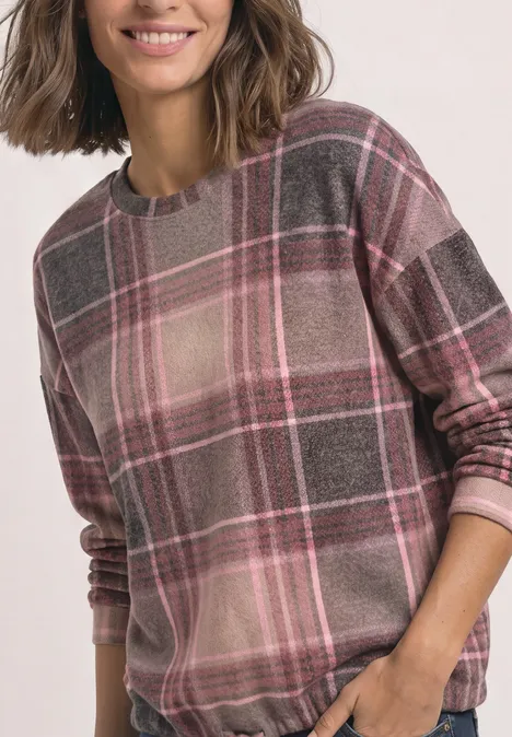 Frau trägt langärmeligen Pullover mit rosa-grauem Karomuster.