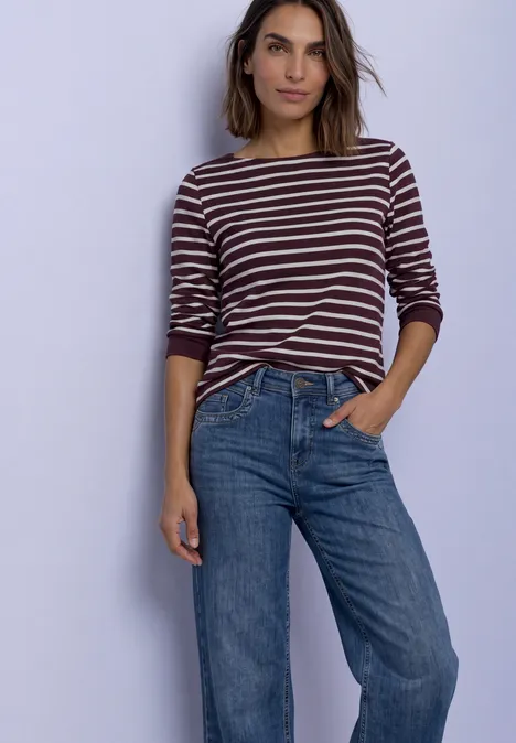Koszulka z rękawami 3/4, dekoltem w łódkę i w paski rustic rouge Kobieta w pasiastym longsleeve i niebieskich dżinsach stoi swobodnie z jedną ręką w kieszeni.
