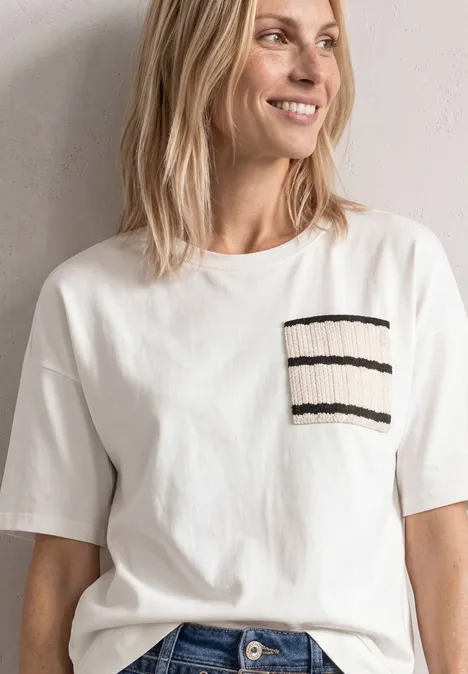 Frau in weißem T-Shirt mit kurzem Arm und aufgesetzter Brusttasche mit schwarzen Streifen, lächelnd.