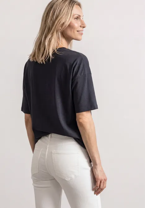 Frau in schwarzem T-Shirt und weißen Jeans, seitlich stehend, Blick nach links.