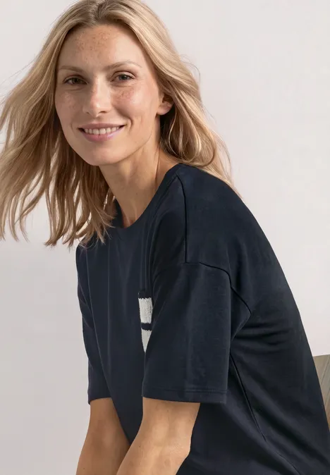 Lächelnde blonde Frau in dunklem T-Shirt sitzt leicht seitlich und schaut in die Kamera.