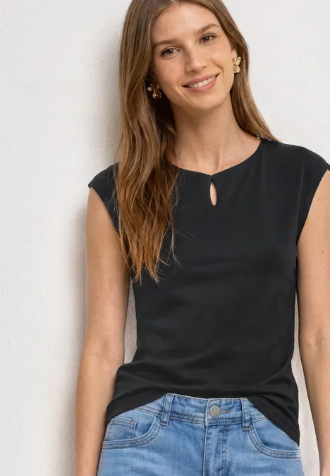 Dropped Shoulder Shirt mit Cut-Out Black Frau in schwarzem ärmellosem Oberteil und Jeans vor weißer Wand