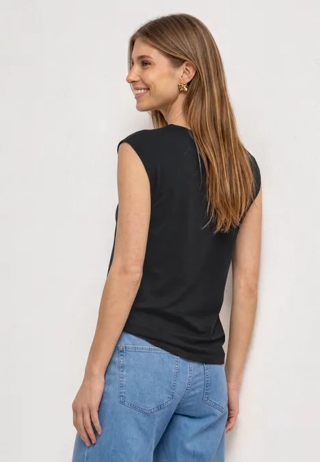 Dropped Shoulder Shirt mit Cut-Out Black Frau von hinten in schwarzem Top und blauen Jeans vor neutralem Hintergrund.