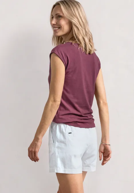 Eine Person steht mit dem Rücken zur Kamera, trägt ein bordeauxfarbenes T-Shirt und weiße Shorts.