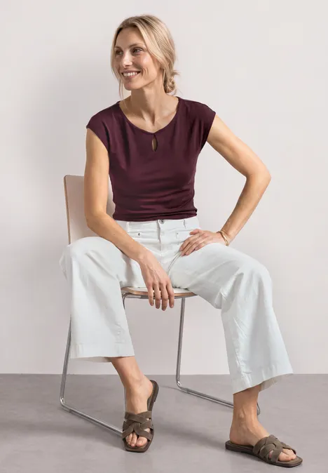 Femme assise sur chaise métallique, portant un top bordeaux, pantalon blanc ample et sandales plates