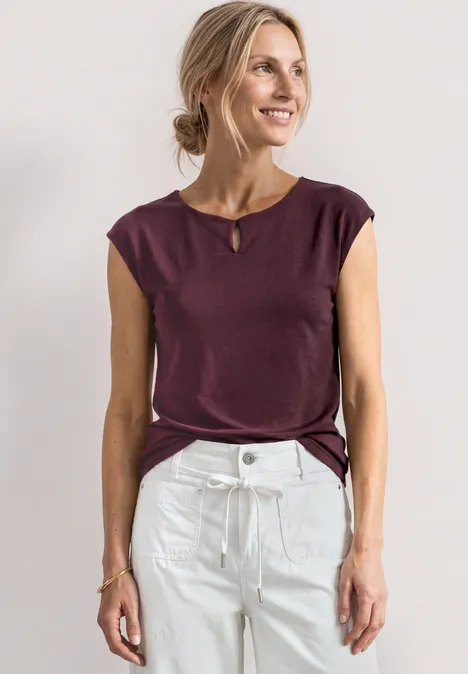 Femme en top bordeaux sans manches et jean taille haute blanc sur fond clair