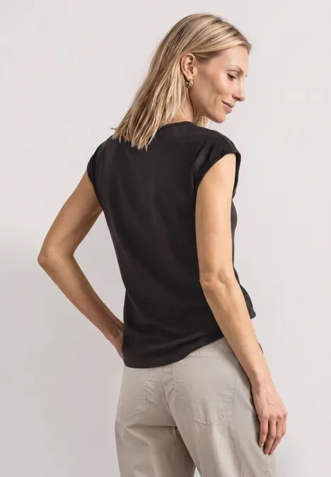 Dropped Shoulder Shirt mit Cut-Out black coffee Frau in schwarzem T-Shirt und beigen Hosen steht mit dem Rücken zur Kamera.