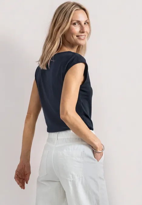Dropped Shoulder Shirt mit Cut-Out darkest blue Eine Frau steht rückwärts, trägt ein schwarzes T-Shirt und weiße Hose, die Hände in den Taschen.