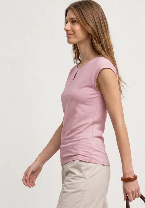 Seitliches Profil einer Frau in rosa ärmellosem Top und beiger Hose vor unifarbenem Hintergrund.