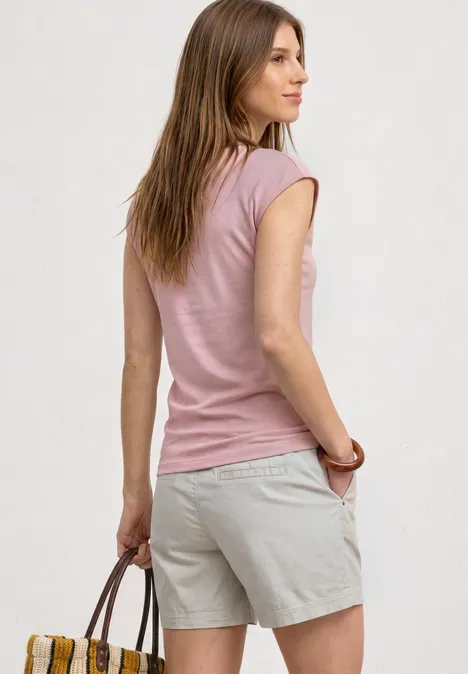 Frau von hinten in einem rosa T-Shirt und beigen Shorts, hält eine braune Handtasche vor hellem Hintergrund.