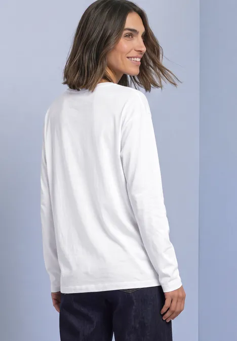 Basic Langarm Shirt in Unifarbe White Frau mit schulterlangen Haaren trägt weißes Langarmshirt, steht seitlich und schaut über die Schulter.