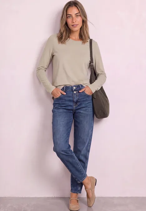 T-shirt basique à manches longues, couleur unie clay sand Junge Frau in beige Longsleeve, blauen Jeans und Loafers lehnt entspannt vor hellrosa Wand.