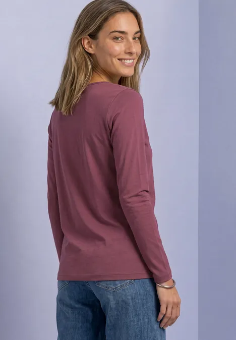 Femme souriante en shirt à manches longues violet et jean regarde par-dessus l’épaule sur fond clair