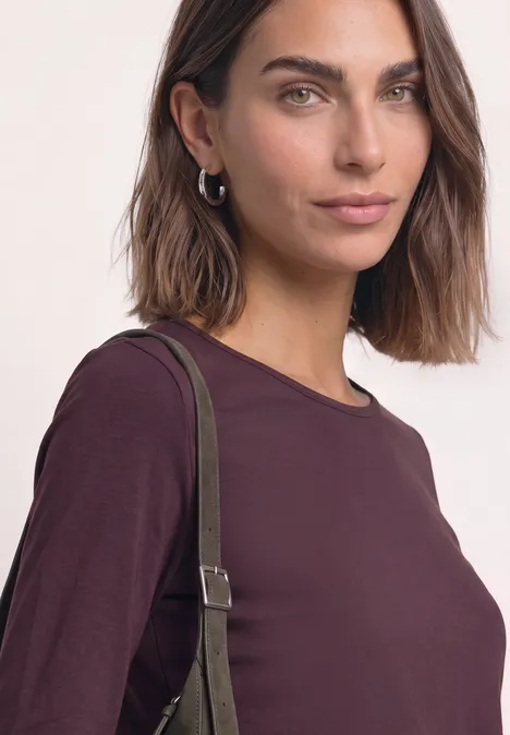 Jednokolorowa koszulka Basic z długim rękawem rustic rouge Portret kobiety w bordowej bluzce z długim rękawem i zielonym paskiem torby na ramię.