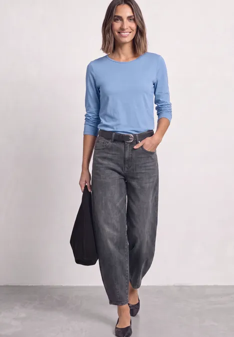 Jednokolorowa koszulka Basic z długim rękawem northern blue Kobieta w niebieskiej bluzce z długim rękawem, luźnych czarnych dżinsach i czarnych butach, trzyma torebkę.