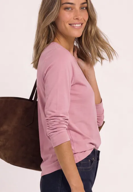 Jednokolorowa koszulka Basic z długim rękawem vintage blush Kobieta w różowej bluzce z długimi rękawami i brązową torbą na ramieniu, uśmiecha się.