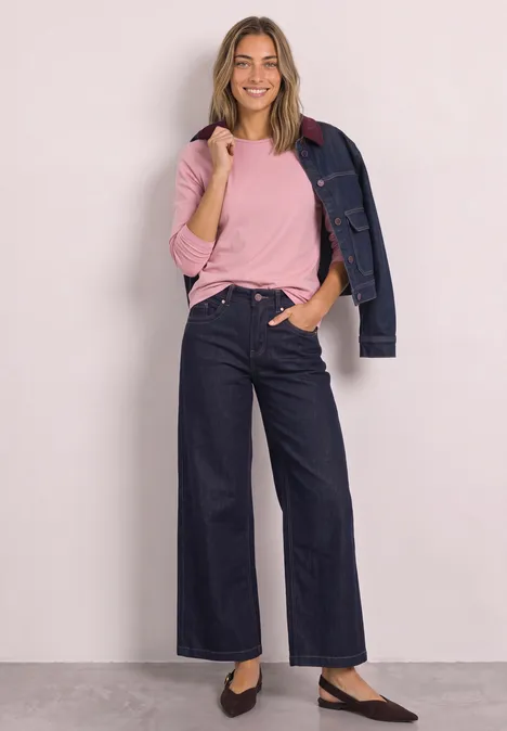Jednokolorowa koszulka Basic z długim rękawem vintage blush Kobieta w różowym T-shircie, dżinsowej kurtce na ramieniu, szerokich ciemnych dżinsach i balerinach.