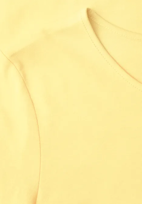 Lichtgeel T-shirt, close-up van de hals en schouder.