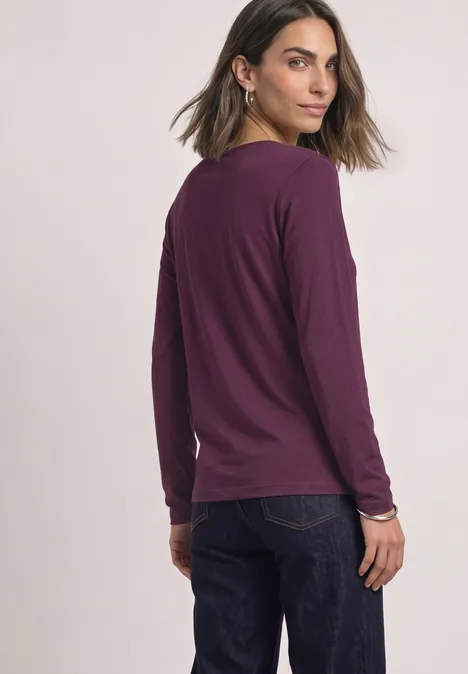 Basic longsleeve berry maroon Vrouw in paars shirt met lange mouwen en jeans kijkt over haar schouder.