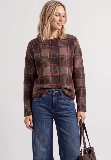 Femme porte un haut à carreaux, un jean bleu et tient un sac à main.
