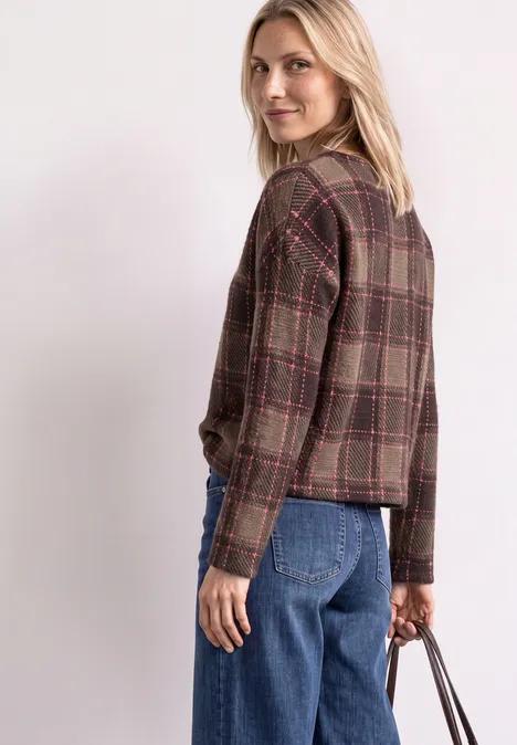 Une femme porte une veste à carreaux brune, un jean bleu, tient un sac à main et regarde par-dessus son épaule.