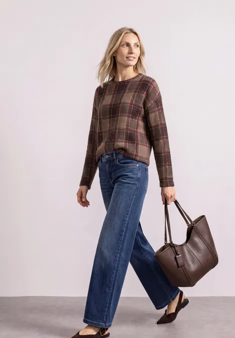 Femme en chemise à carreaux, jean large et sac en cuir marron sur fond clair.