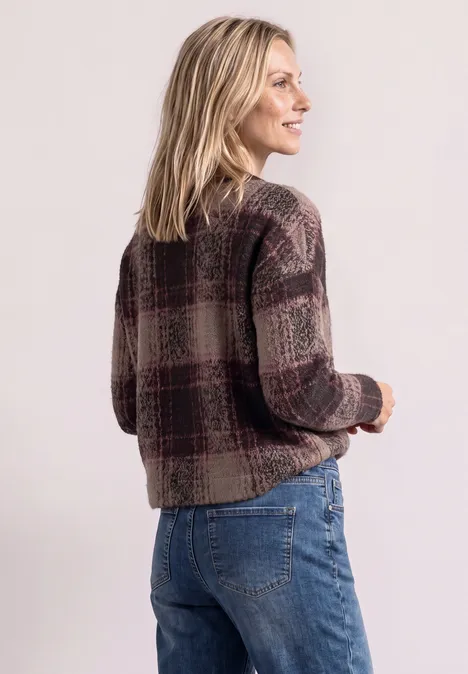 Une femme blonde en cardigan à carreaux et jean regarde de côté en souriant.