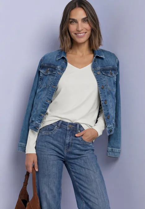 Koszulka z długim rękawem i dekoltem w kształcie kwadratu off white Uśmiechnięta kobieta pozuje na jasnym tle w dżinsowej kurtce, białym t-shircie i niebieskich dżinsach