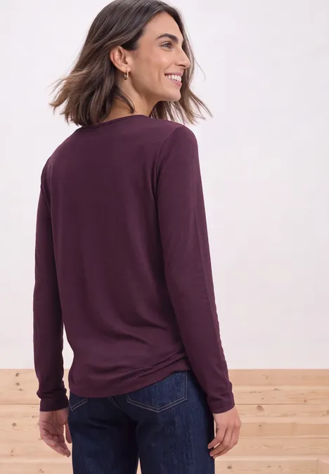 Shirt met lange mouwen en vierkante halslijn berry maroon Frau von hinten, trägt bordeauxrotes Langarmshirt und Jeans, blickt lächelnd über die Schulter.