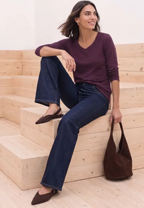 Shirt met lange mouwen en vierkante halslijn berry maroon Frau sitzt entspannt auf Holzstufen, trägt Jeans, pflaumenfarbenes Langarmshirt und spitze Schuhe, hält Handtasche.