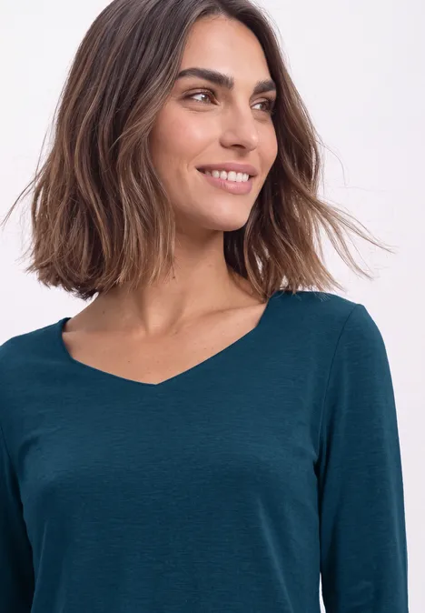 Frau mit schulterlangem braunem Haar und dunkelgrünem V-Ausschnitt-Shirt lächelt seitlich.