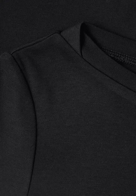 Gros plan d’un vêtement noir montrant l’encolure ronde et la couture de la manche.