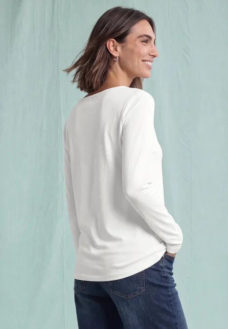 Langarm Shirt mit U-Boot-Ausschnitt off white Eine Frau in weißem Langarmshirt und Jeans blickt lächelnd seitlich über die Schulter vor hellem Hintergrund.